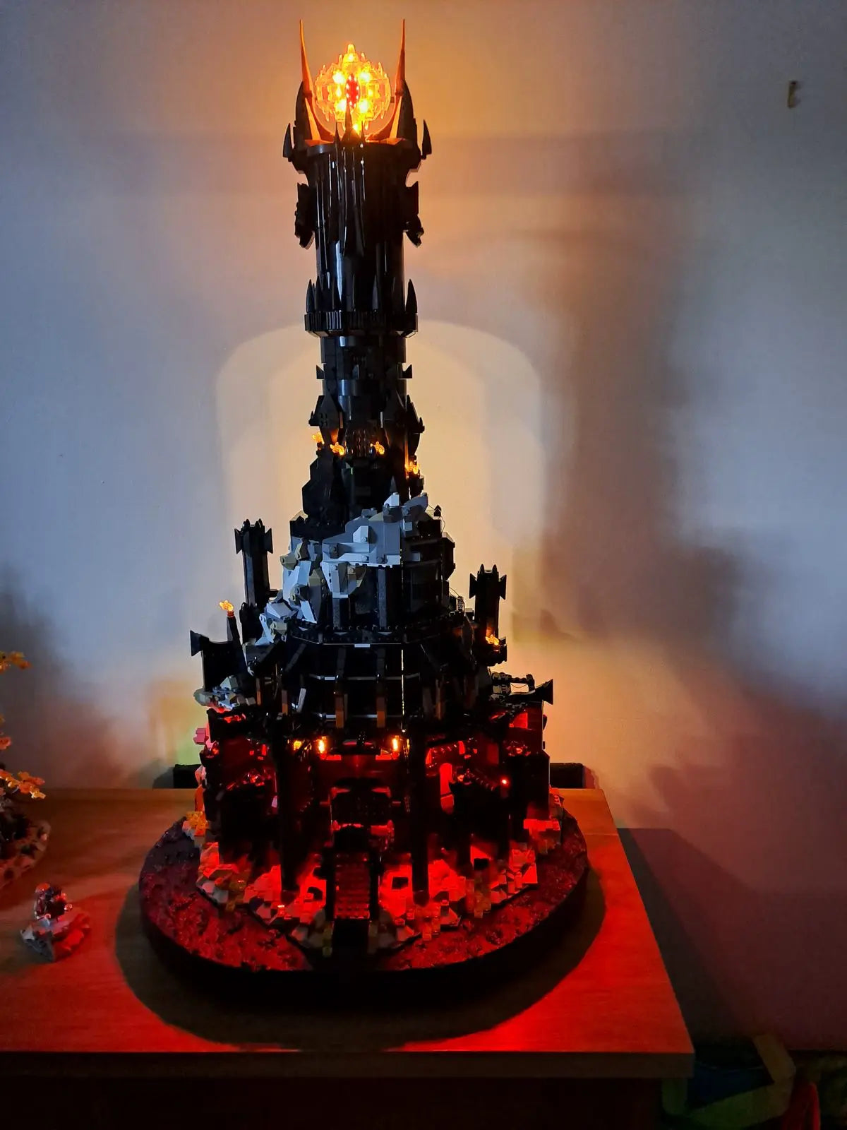 Impressive LEGO Barad-dûr tower from Lord of the Rings (set 10333) with custom LED lighting system. The massive 5471-piece dark fortress rises majestically with Sauron's Eye illuminated in orange and red at the summit. The base features dramatic red lighting simulating the fires of Mordor, creating a dark and menacing atmosphere perfect for this replica of Sauron's tower from Middle-earth.