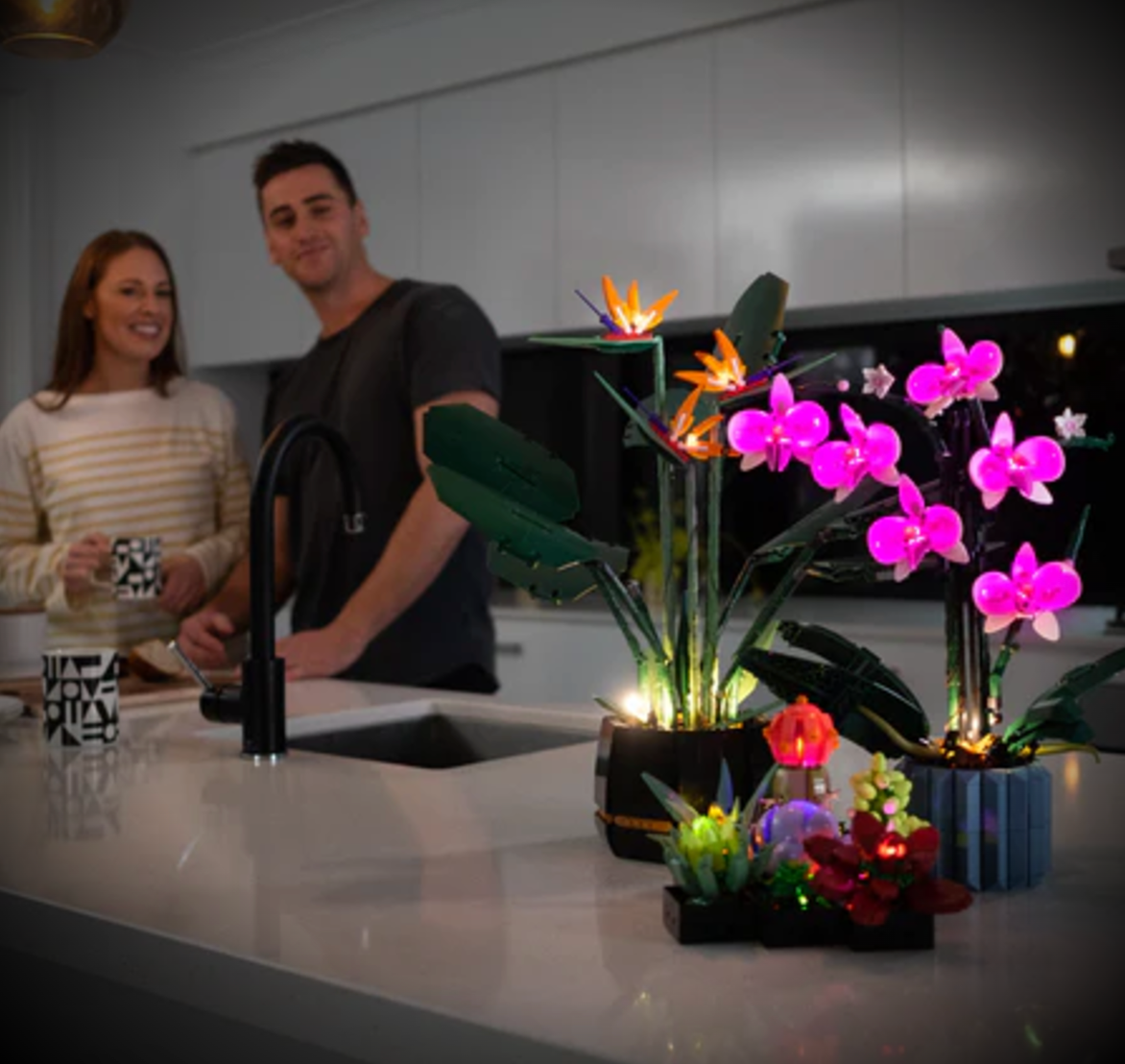 Couple enjoying their illuminated LEGO® Botanical sets with BrightMyBricks LED Lighting Kits in a modern kitchen.