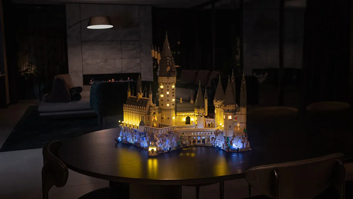 Professional showcase of multiple illuminated LEGO sets featuring custom LED lighting installations by skilled technician. The collection displays various iconic builds including the towering Barad-dûr with dramatic orange Eye of Sauron, the colorful Disney Encanto Casa Madrigal with multicolor lighting effects, the massive Millennium Falcon UCS with blue engine illumination, and the mystical Rivendell with warm golden and blue lighting accents. Each set demonstrates expert custom lighting work that transforms standard LEGO builds into stunning display pieces, perfect for collectors and enthusiasts seeking professional lighting enhancement services for their LEGO collections. The warm ambient lighting creates an inviting atmosphere that highlights the intricate details and craftsmanship of both the original LEGO designs and the custom lighting installations.