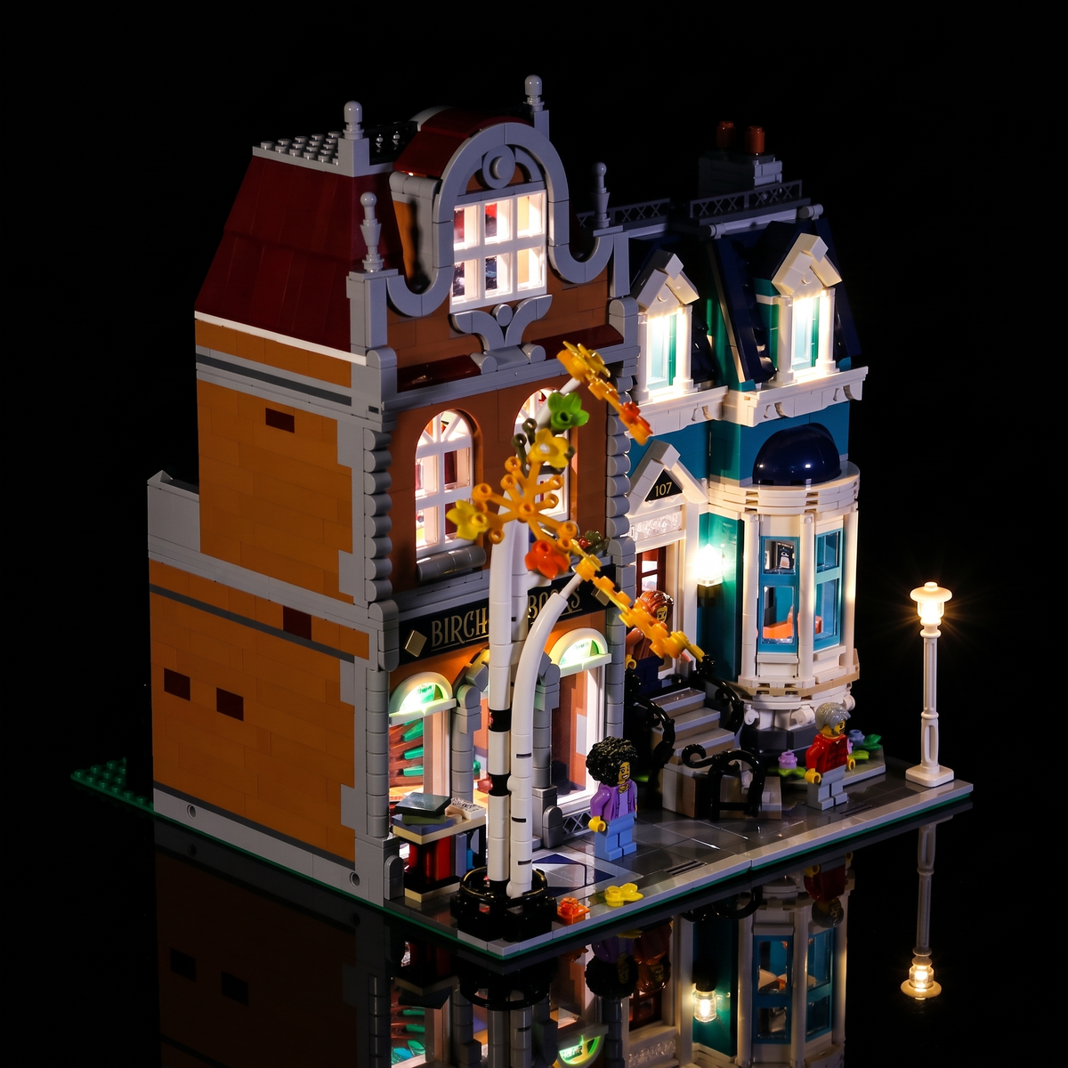 Linke Vorderansicht der beleuchteten LEGO Buchhandlung 10270 mit Birke, Schaufenstern und Straßenlaterne