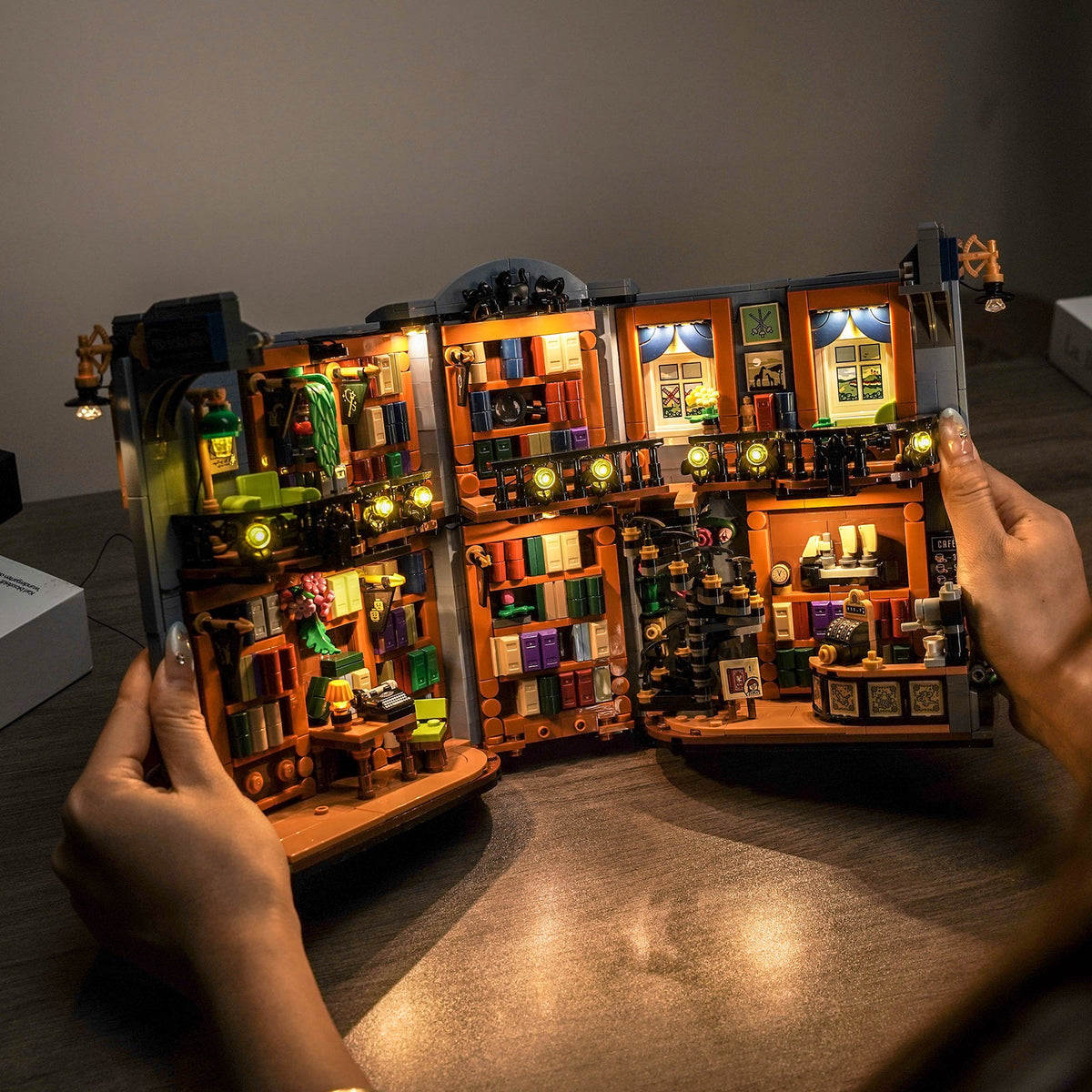 LEGO® Icons La librairie : book nook #11379 ouvert et tenu en main avec éclairage LED chaud sur les deux étages